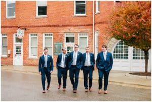 A groom and his groomsmen walk down the street and in the rain together.