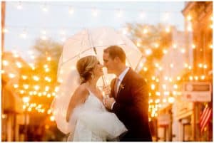 A husband and wife taking shelter from the rain under a white umbrella.