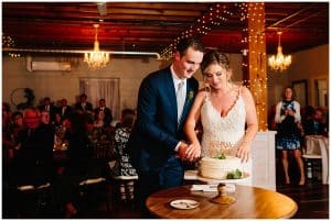 A bride and groom cut the cake at their wedding and stand close to each other.