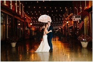 Bride and groom standing under the twinkling lights in the rain.