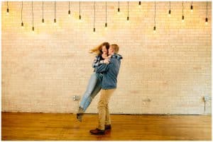 A young man swings his fiancee around under some hanging lights
