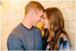 An engaged couple laughs and smiles at each other as they lovingly lean on each other.
