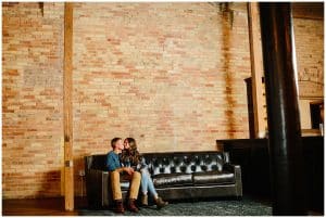 A couple sits on a victorian looking sofa and leans in to kiss one another.