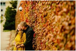 An engaged couple standing next to a wall of brightly colored leaves.