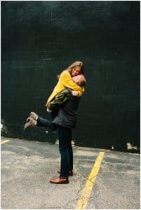 A young man lifts up his fiancee and holds her close as she hangs tight to his neck and smiles.