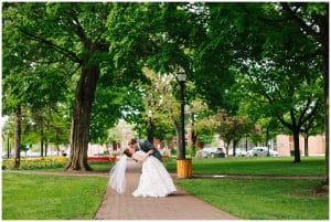 A groom takes his bride and dips her as he gives her a kiss in the middle of a park.
