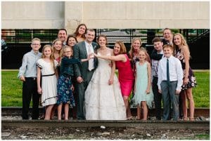 A bride and groom take a group family shot in front of some railroad tracks.