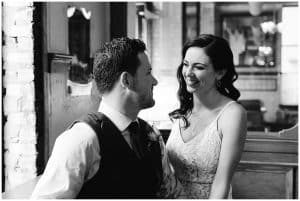 A bride and groom sit inside a french styled building and smile at each other before the wedding ceremony.