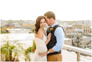 A soon to be married couple poses on top of a roof with the Grand Rapids skyline behind them.