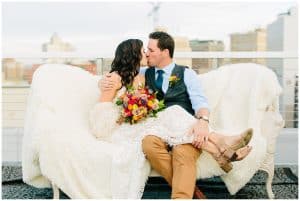 A bride sits with her legs over her groom as they cuddle close on an antique couch.