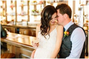 A bride and groom sit close together at a bar.