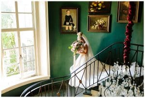 Picture of a bride walking down the stairs to meet her groom for the ceremony; they are at an estate.