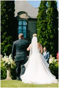 A bride walking down the aisle with her father during her outdoor garden party wedding.