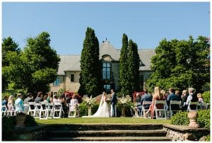 Bride and groom standing in front of a large estate sharing their wedding vows with each other.