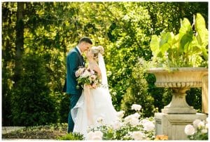 Bride and groom kiss under some trees in a magical looking garden on the site of their wedding.