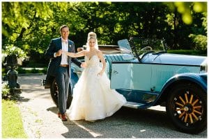 A groom helps his bride as she exists an old vintage car as part of their wedding photo shoot by Mae Photo Co.