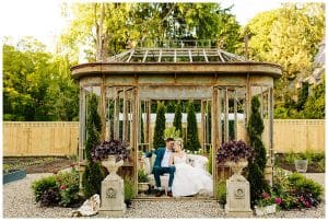 Picture of a married couple cuddling on a small sofa under a vintage gazebo on an estate property.