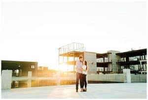 Couple standing on top of a parking garage with the sun setting behind them in downtown GR