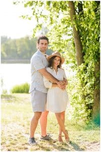 An engaged couple stand next to some trees in the sun as they pose for some engagement pictures in Grand Rapids, Michigan.